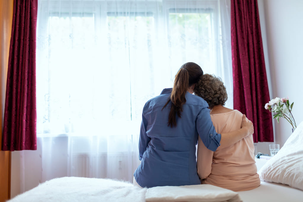 support worker hugging elderly woman on bed