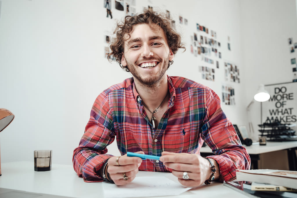 smiling guy sits on a table with a pencil in his hands