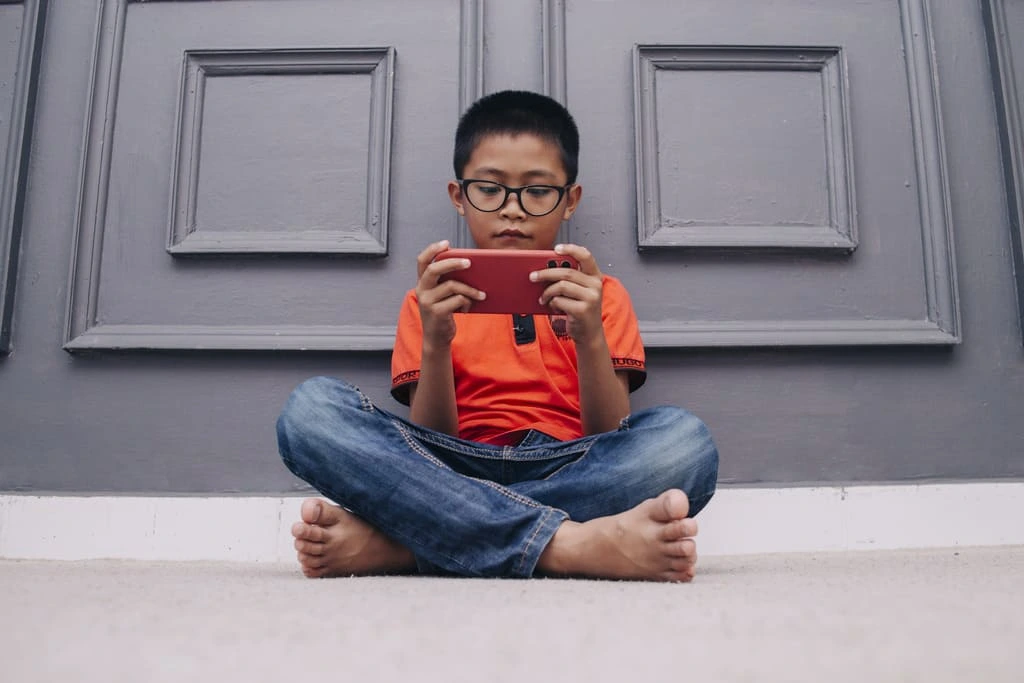 kid sitting in front of the door playing on phone