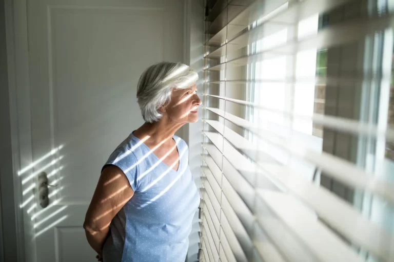 older woman looking through blinds on a window