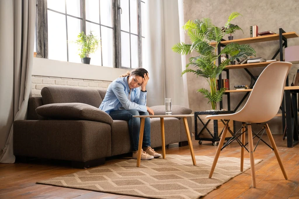 woman sitting on a couch alone holding her head