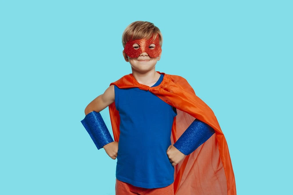 kid posing in a superhero costume with red cape